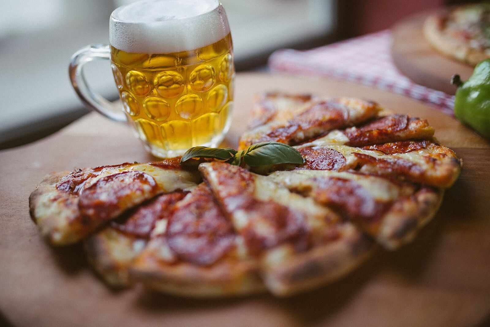 A cold glass of beer beside a sliced pizza