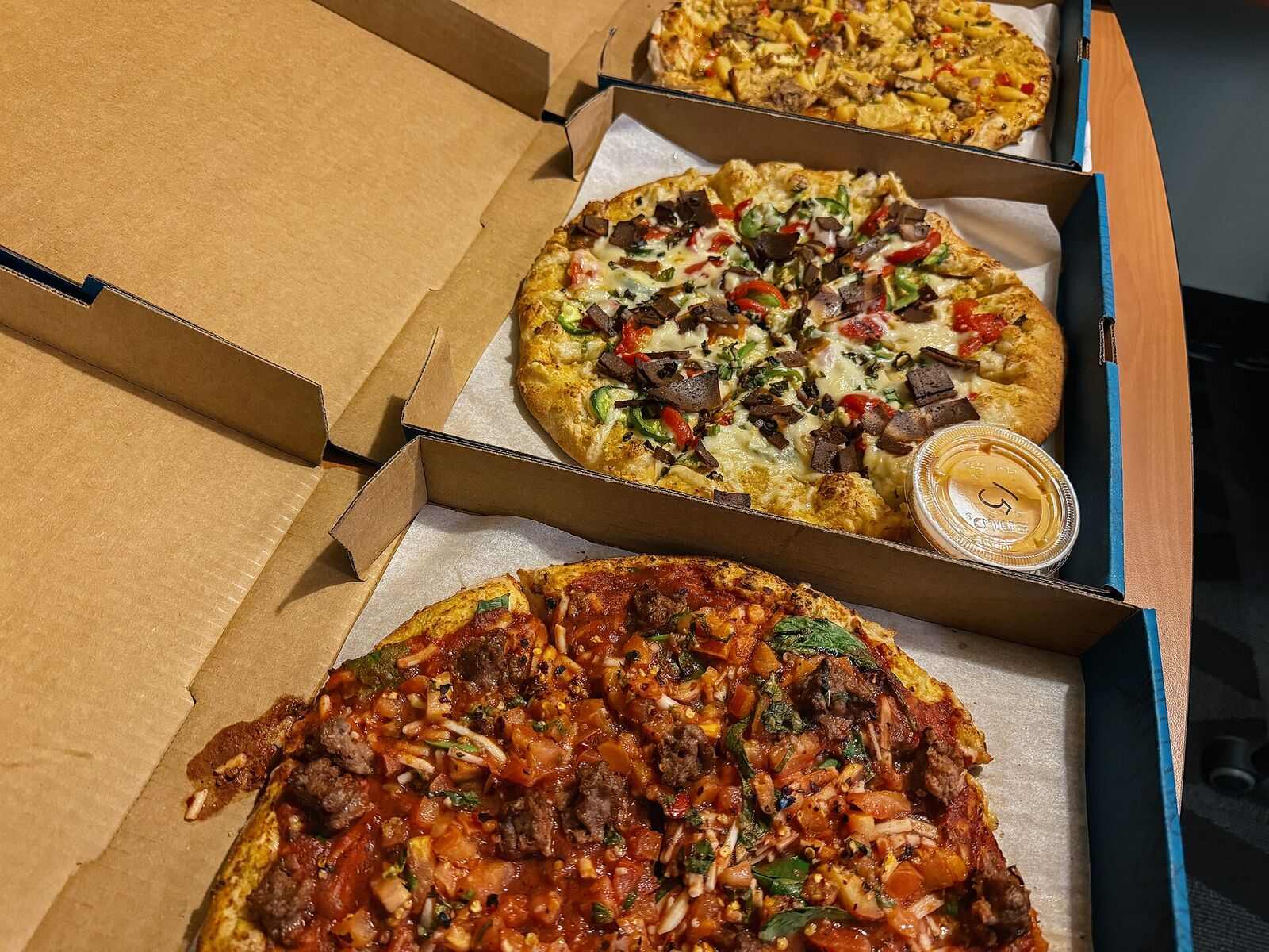 Three open boxes of pizza lined up side by side, ready for a group