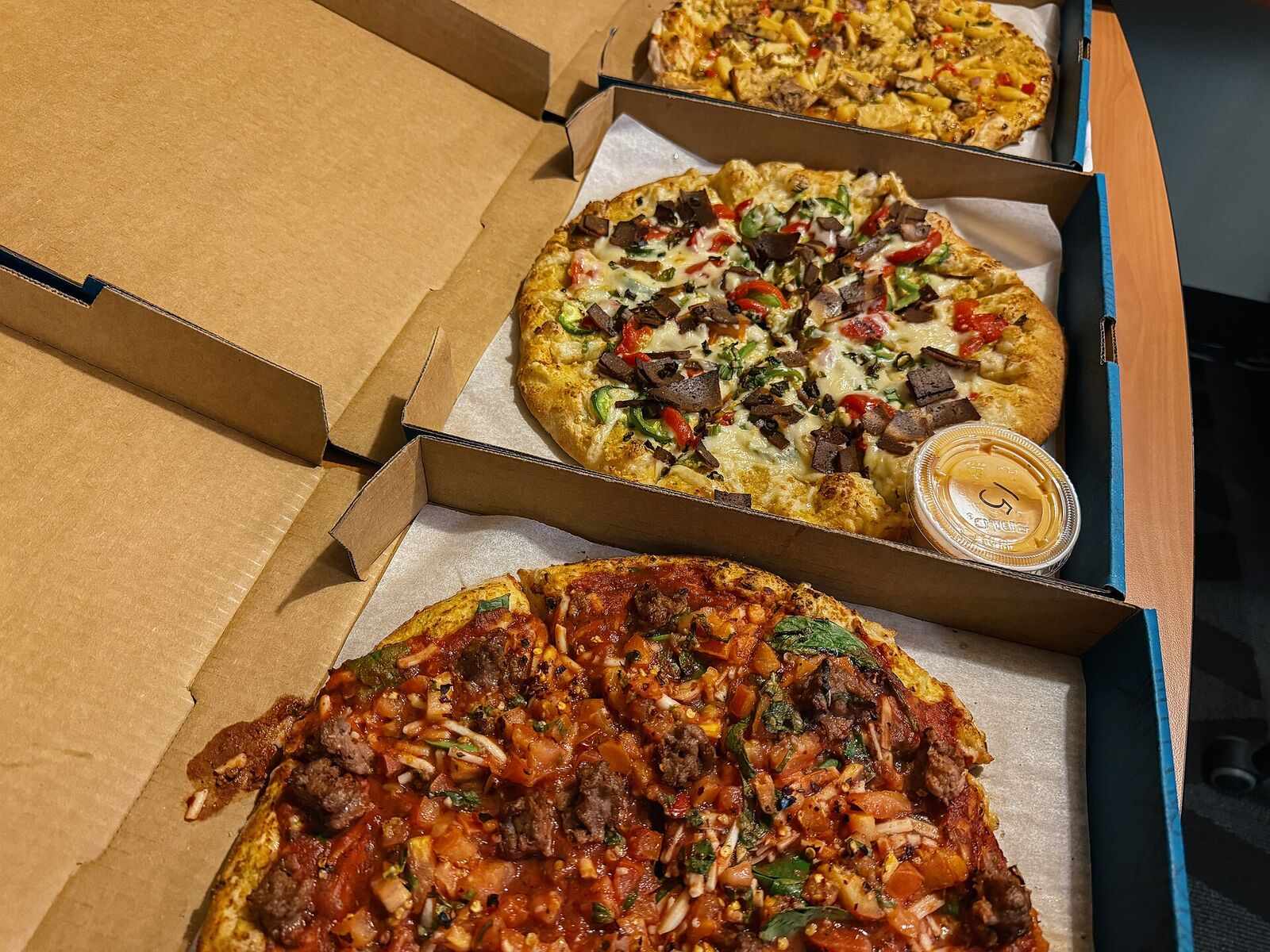 Three open boxes of pizza lined up side by side, ready for a group