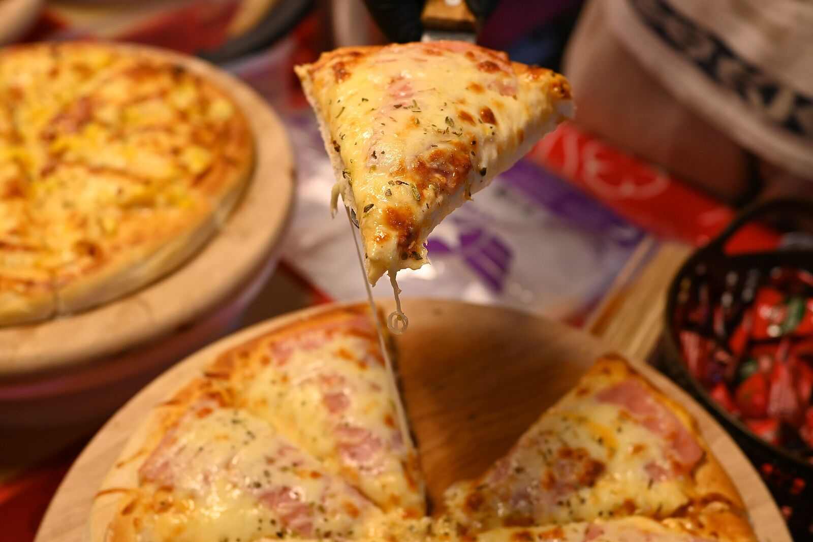Slice being lifted from a pizza on a wooden board, cheese strands stretching