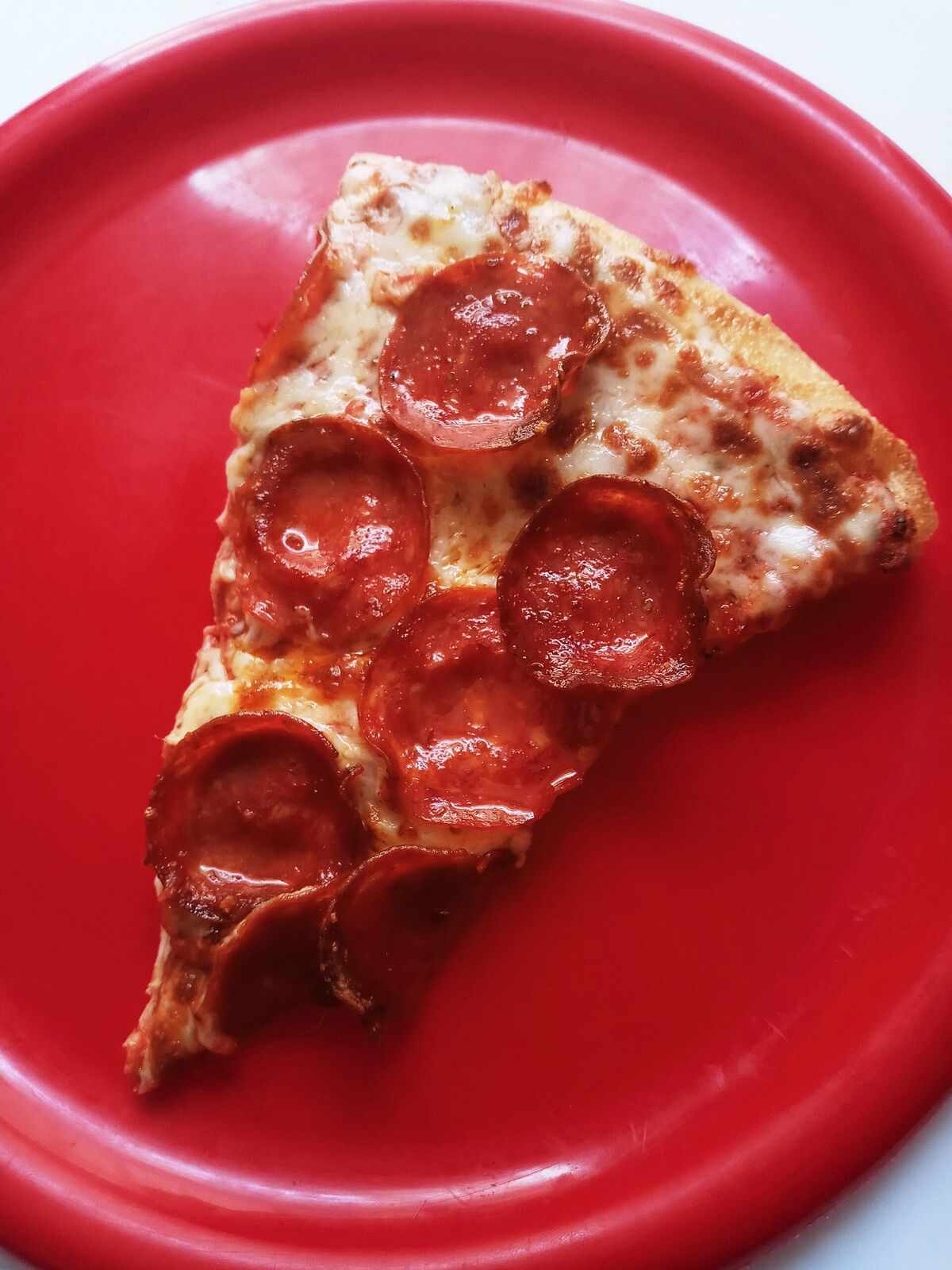 A single pepperoni slice on a bright red plate